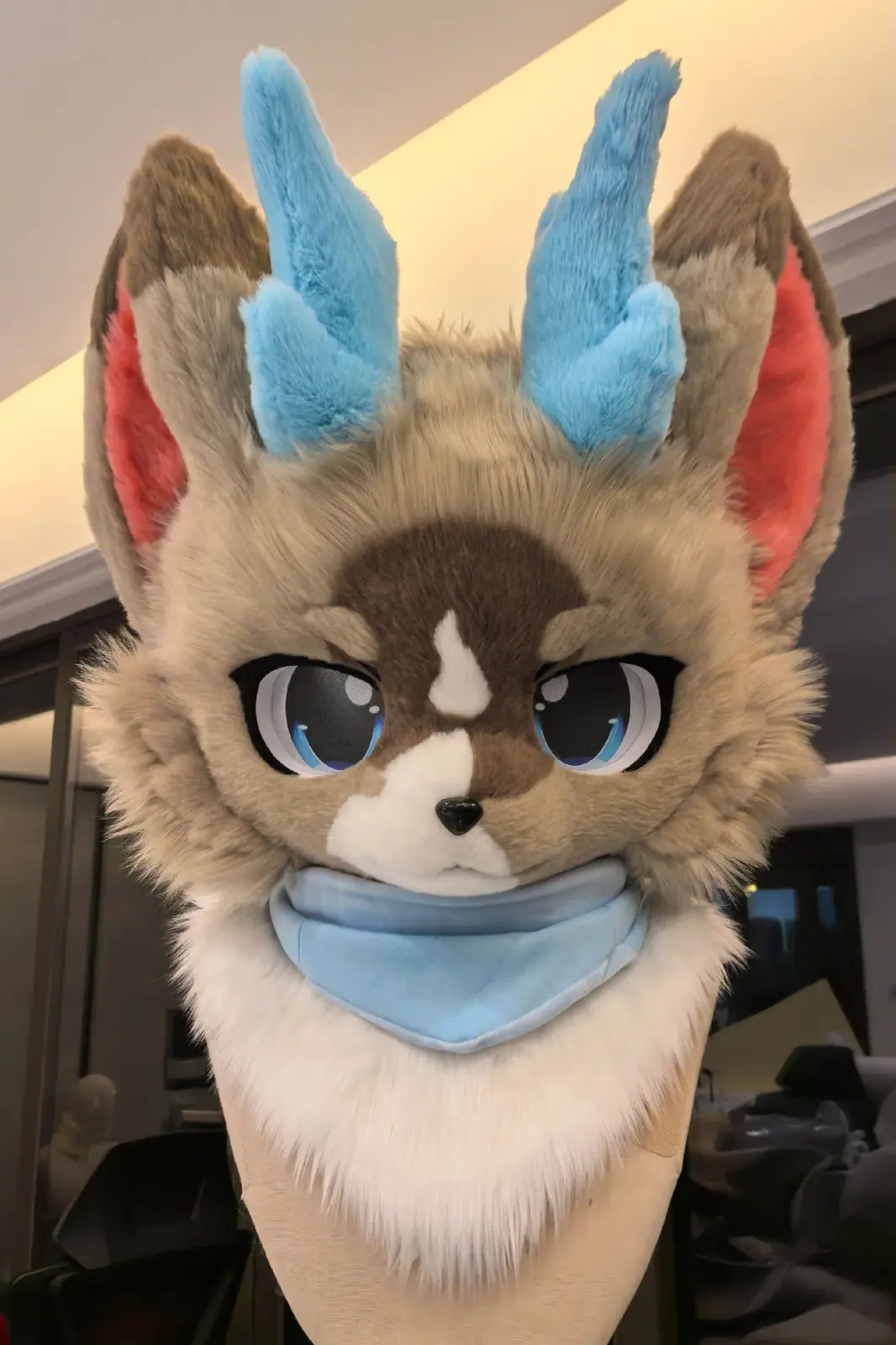 Kemono-style tan and brown fursuit head with sky-blue horns, pink inner ears and a blue bandana, front view with blue eyes