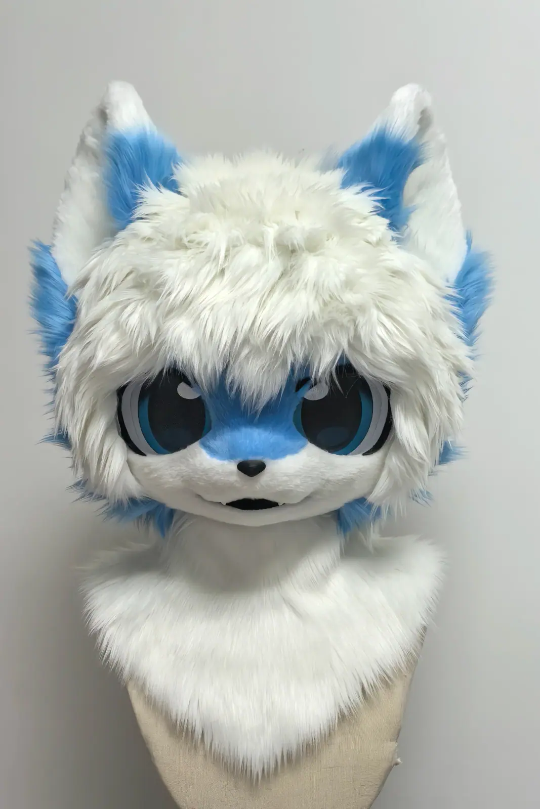 Kemono-style white fursuit head with blue ear tufts, a blue face and big round blue anime eyes, front view