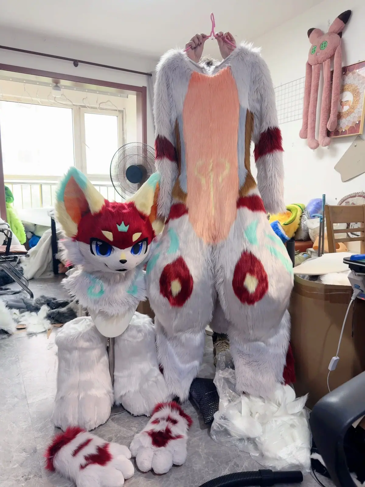 Kemono-style crimson and grey fox fursuit with a teal crown marking, blue anime eyes and red-striped paws, with the digitigrade bodysuit before final assembly