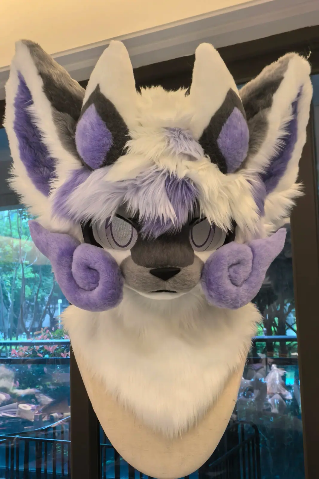 Kemono-style grey and white fursuit with lavender curled horns, purple inner ears and sleepy anime eyes, front view