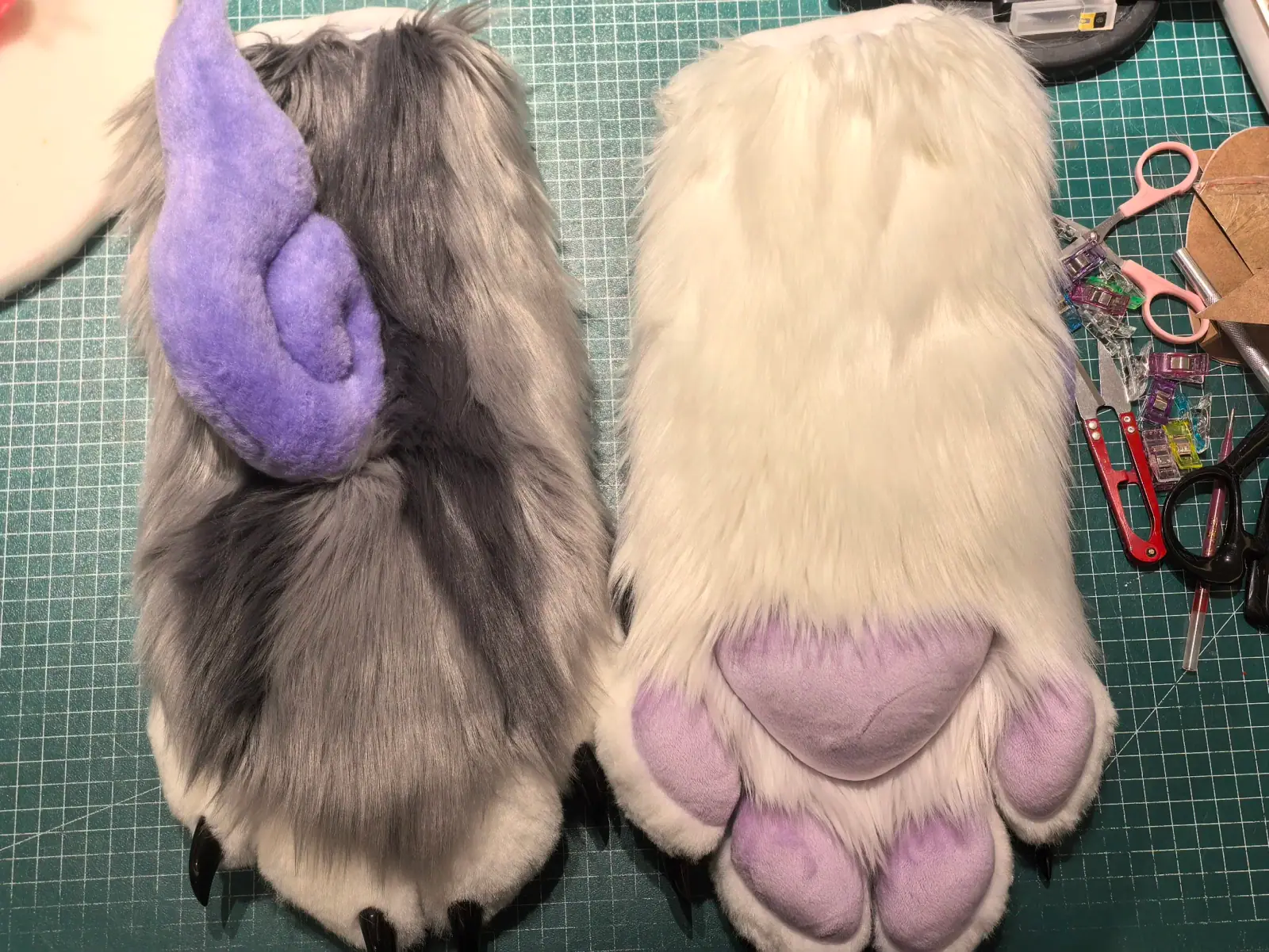 Kemono-style grey and white fursuit with lavender curled horns, purple inner ears and sleepy anime eyes, matching hand paws with lavender paw pads