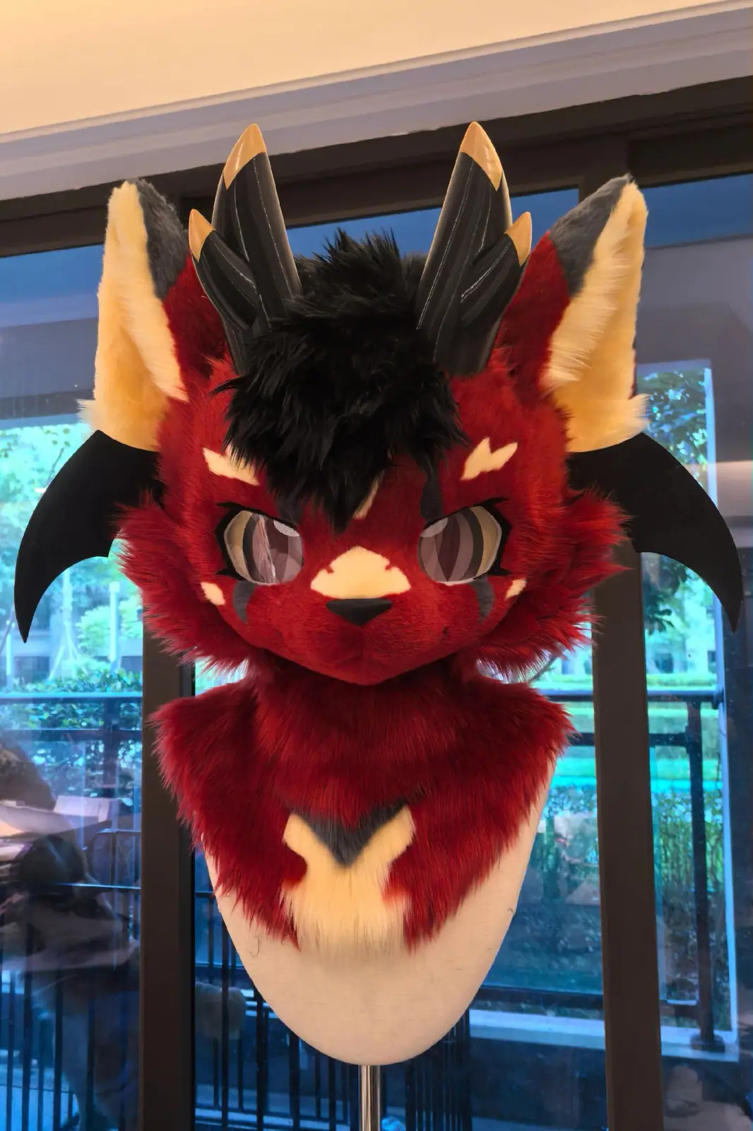 Kemono-style red and black dragon fursuit with black horns and wings, yellow ear tufts and pink anime eyes, front view of the head