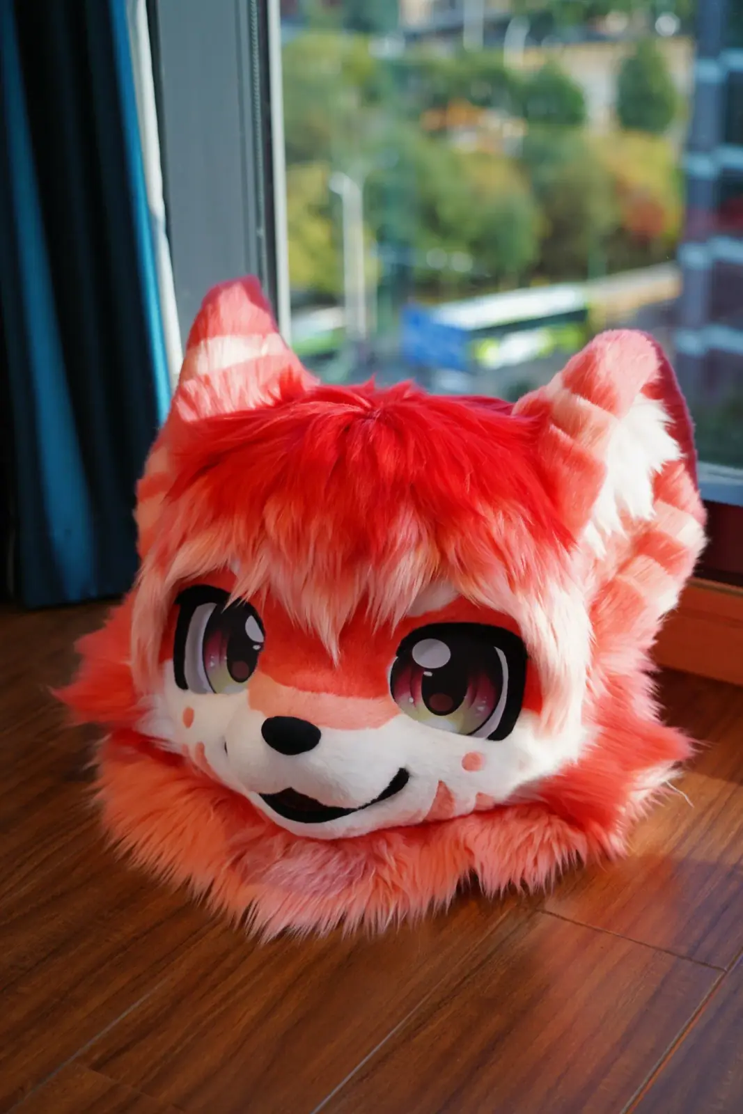 Kemono-style red panda fursuit head with red and pink striped ears, ruby anime eyes and freckled white cheeks, front view