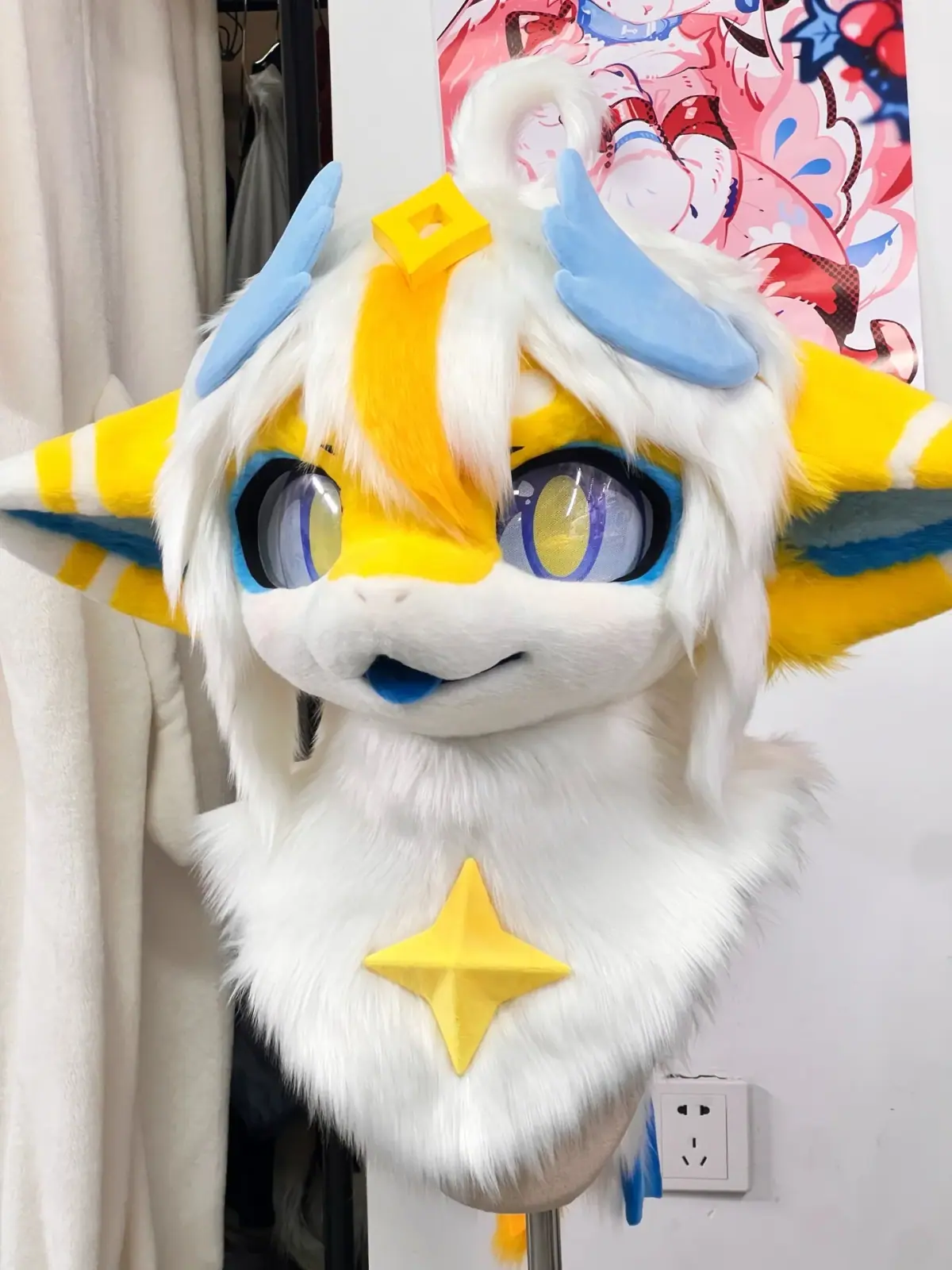 Kemono-style white dragon fursuit head with yellow and blue striped ears, sky-blue horns, large blue and gold anime eyes and a yellow star on the chest ruff, front view on a head stand