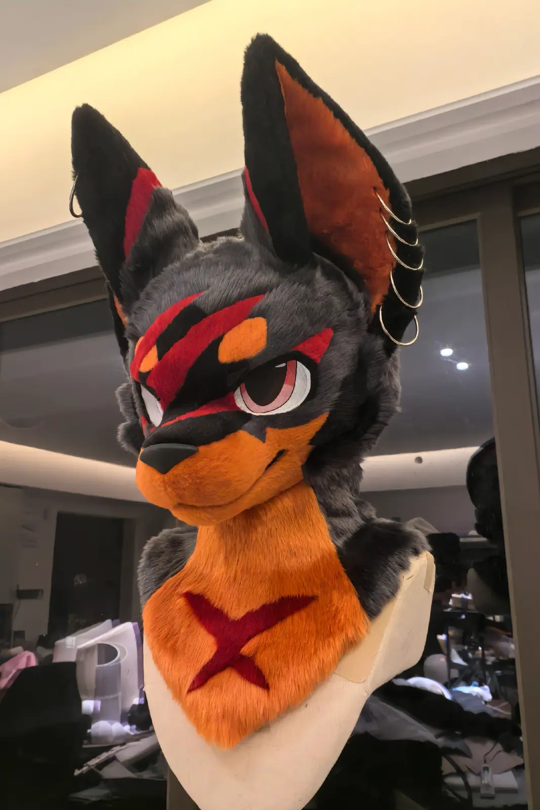 Toony-style black jackal fursuit head with an orange muzzle, red markings, tall ears and an orange bandana, front view