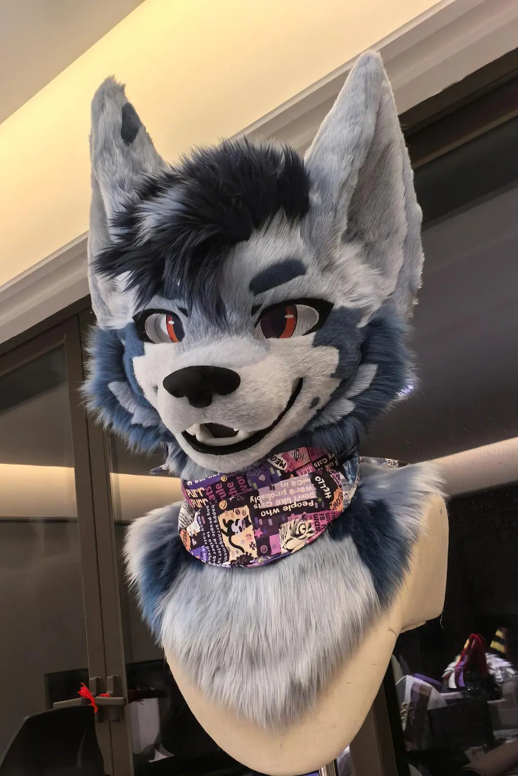 Toony-style blue-grey wolf fursuit head with a dark mane, red eyes, an open smile and a printed bandana, front view