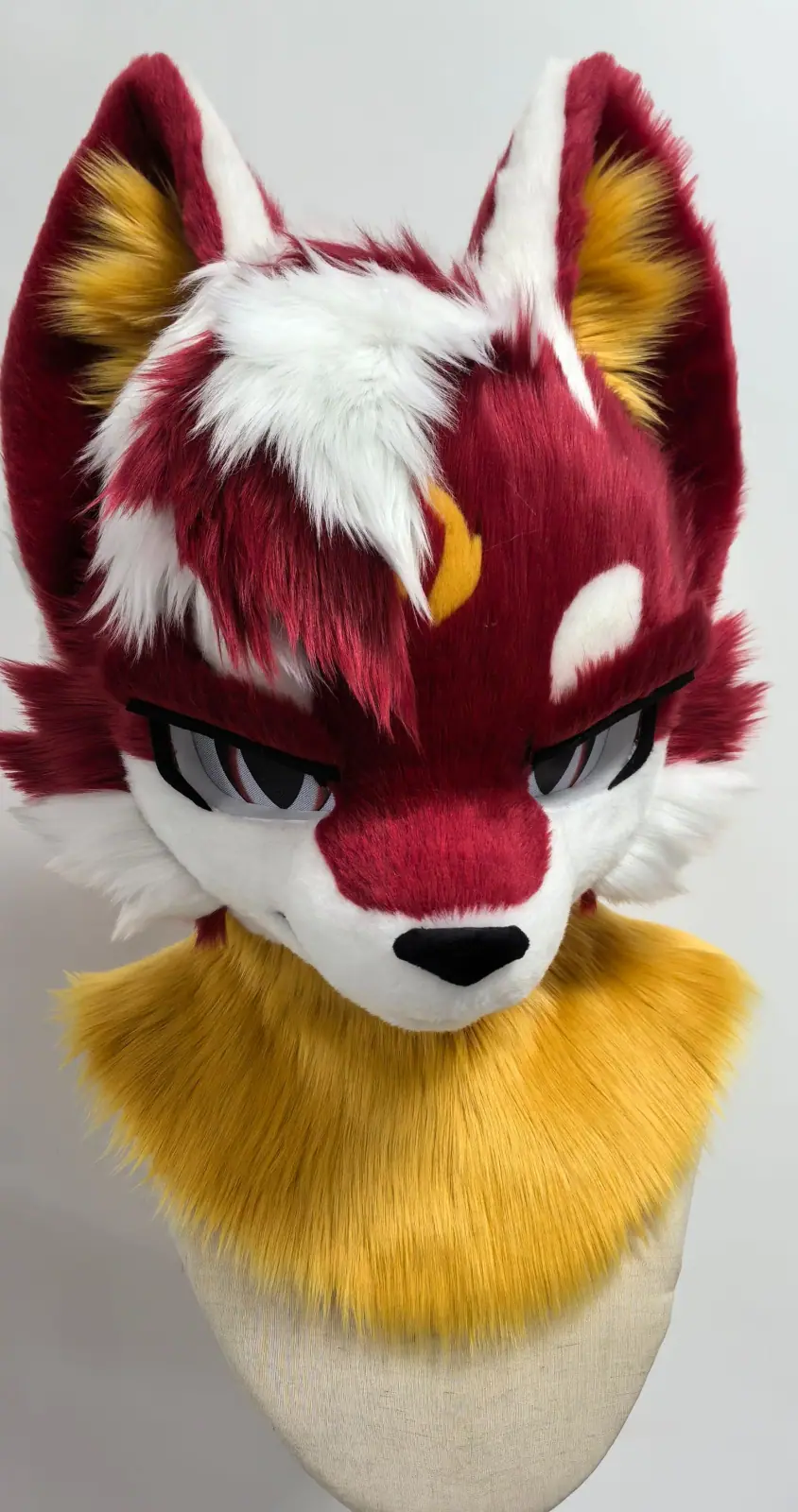 Toony-style crimson and white fox fursuit head with a golden neck ruff and red anime eyes, front view