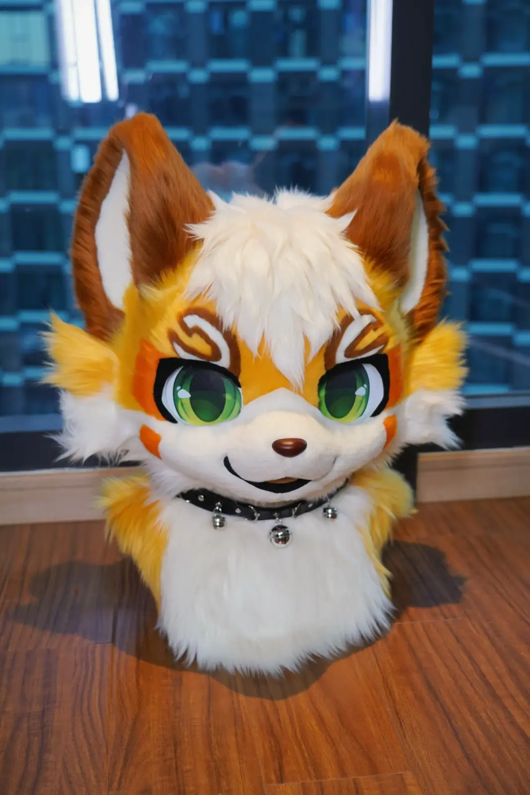 Toony-style golden and white fox fursuit head with brown ears, swirl brow markings, green anime eyes and a bell collar, front view