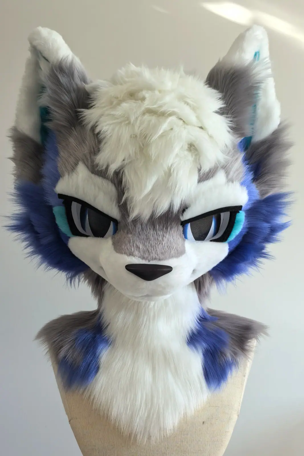 Toony-style grey and white wolf fursuit head with indigo cheek fluff, teal inner ears and blue anime eyes, front view