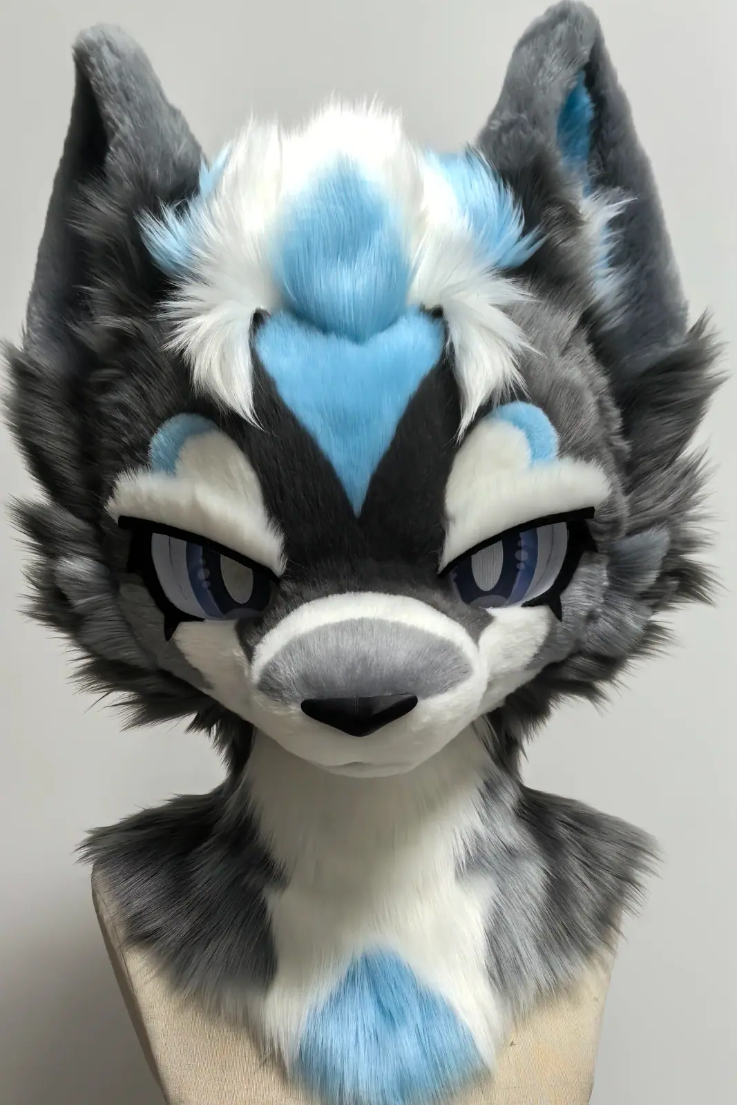 Toony-style dark grey and white wolf fursuit head with a sky-blue heart-shaped blaze and lavender anime eyes, front view