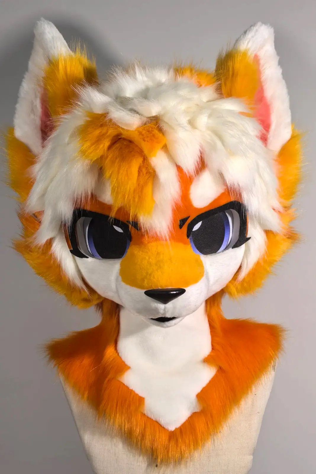 Toony-style orange and white fox fursuit head with yellow fluff, pink inner ears and violet anime eyes, front view