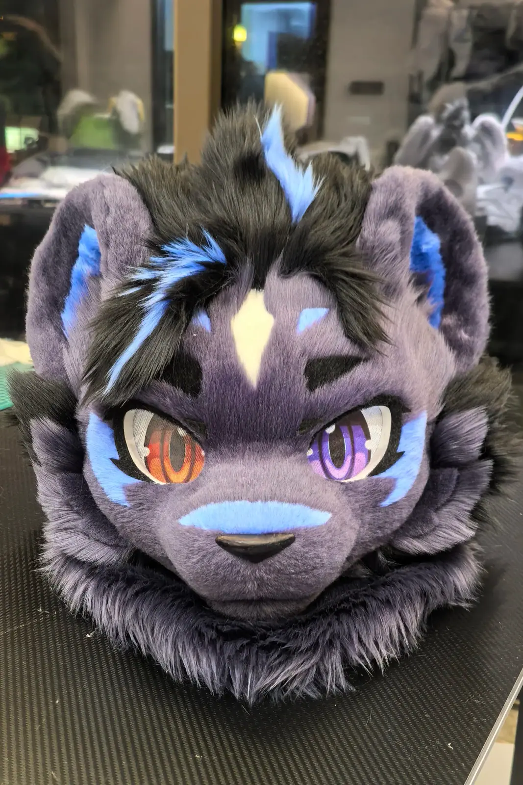 Toony-style purple and black hyena fursuit head with blue streaks and odd orange and violet eyes, front view