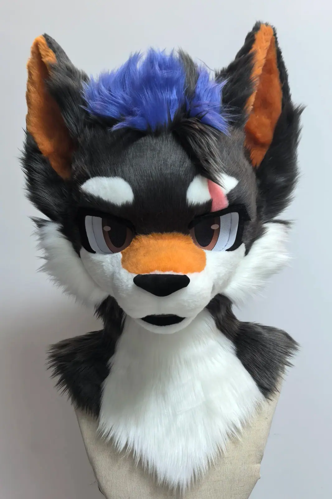 Toony-style black and white wolf fursuit head with a purple mohawk, orange muzzle and inner ears and a pink scar, front view