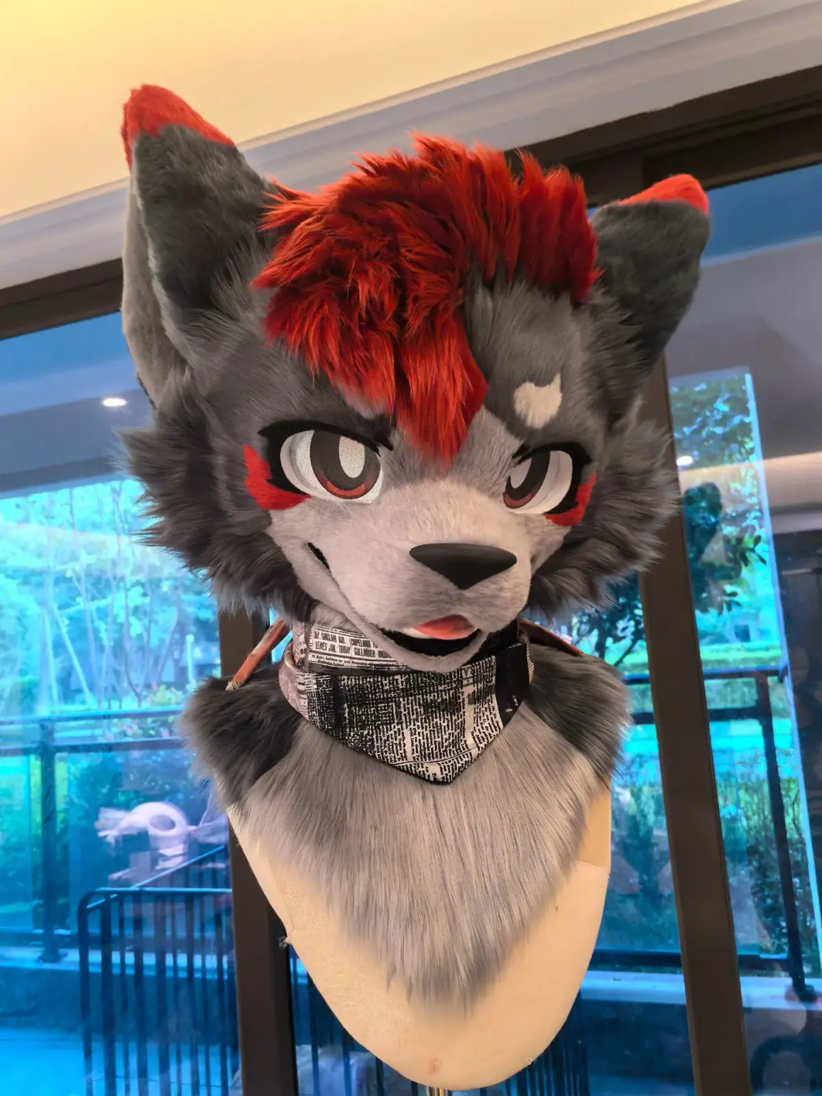 Toony-style grey wolf fursuit head with spiky red hair, red cheek marks and a newspaper-print bandana, front view
