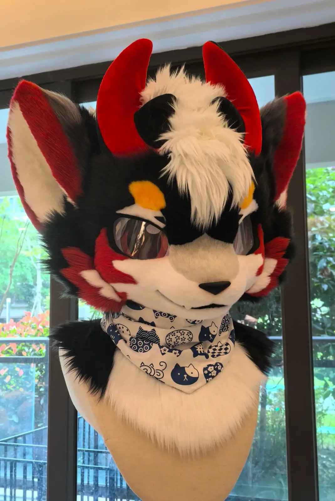 Toony-style black and tan fox fursuit head with red horns, an orange eye patch and a blue paisley bandana, front view