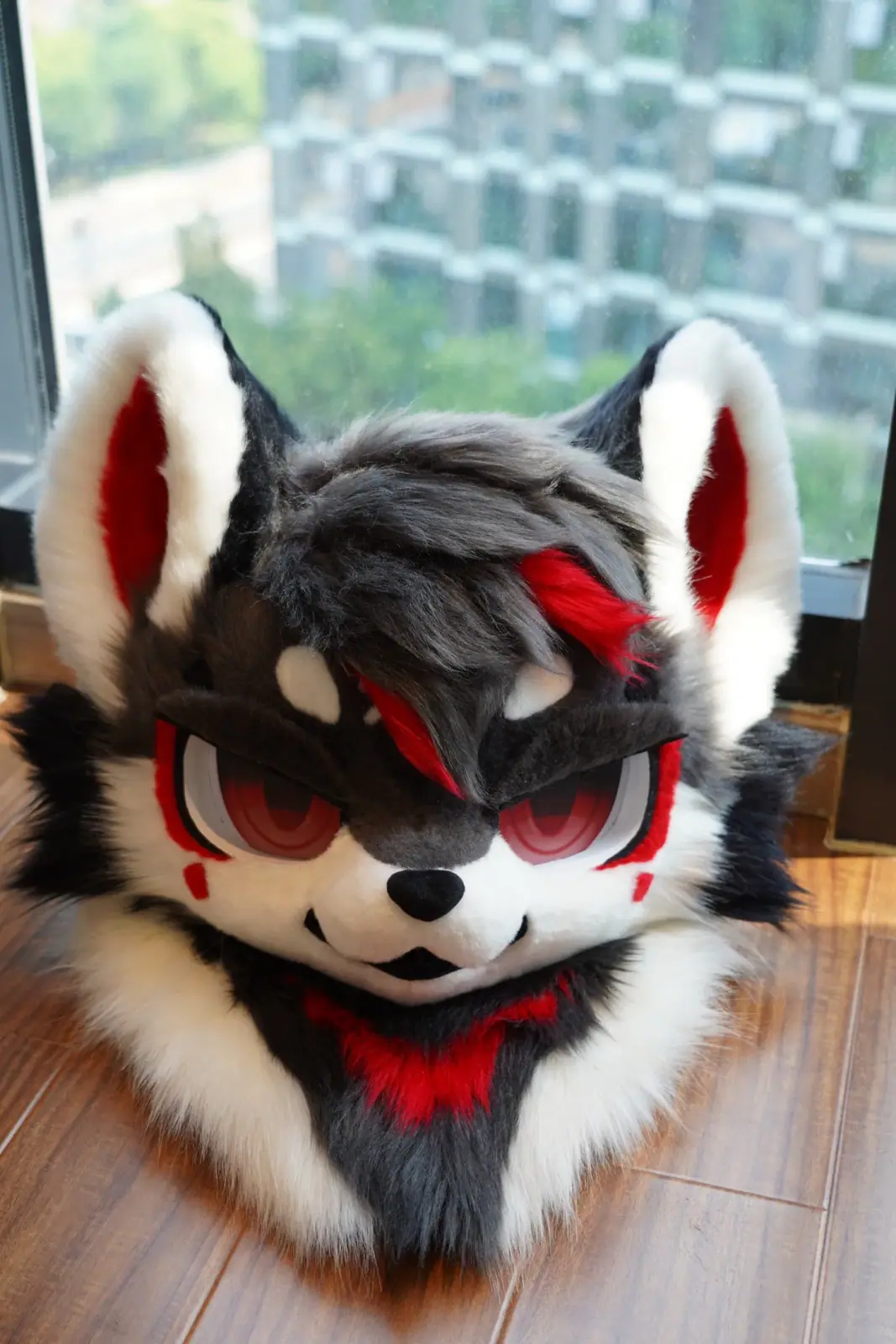 Toony-style charcoal and white wolf fursuit with a red hair streak, red eye markings, red inner ears and matching feet paws, front view
