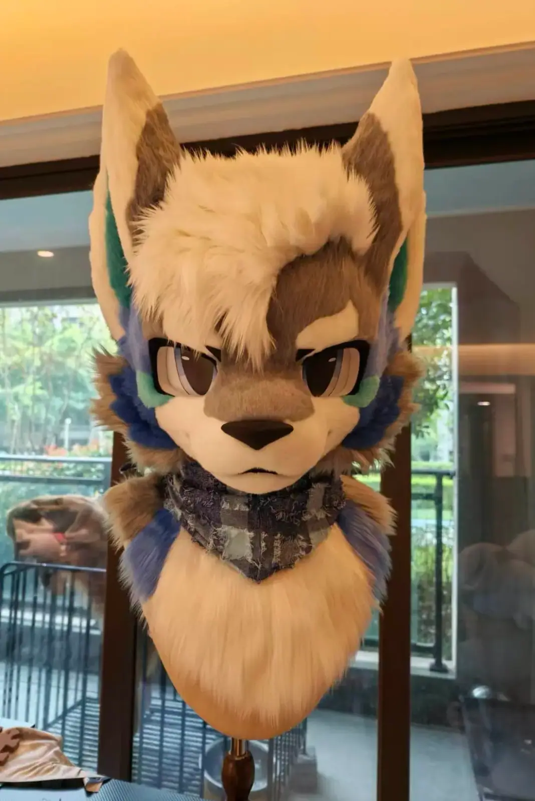 Toony-style tan and brown wolf fursuit head with teal inner ears, purple accents and a plaid bandana, front view