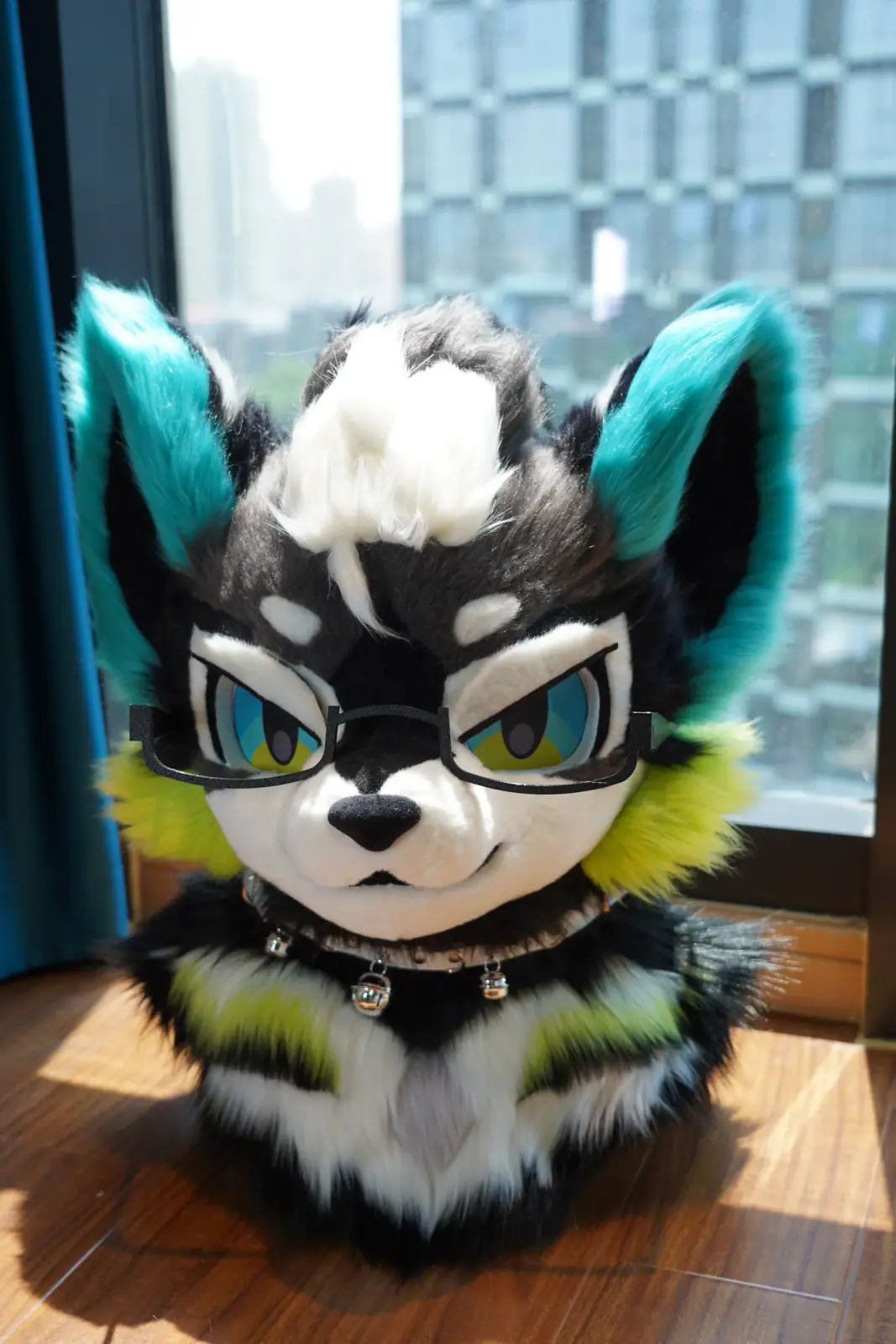 Toony-style black and white husky fursuit head with teal ears, lime cheek fluff, blue and yellow anime eyes and a studded bell collar, front view