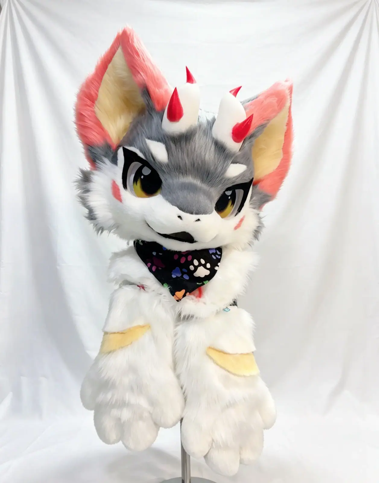 Kemono-style grey and white horned dragon fursuit with coral ears, red-tipped horns, golden anime eyes and a paw-print bandana, three-quarter view